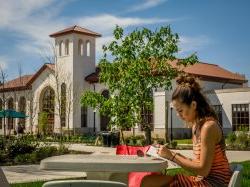 Photo of student highlighting content in book while sitting at an outside table on campus on a sunny day.