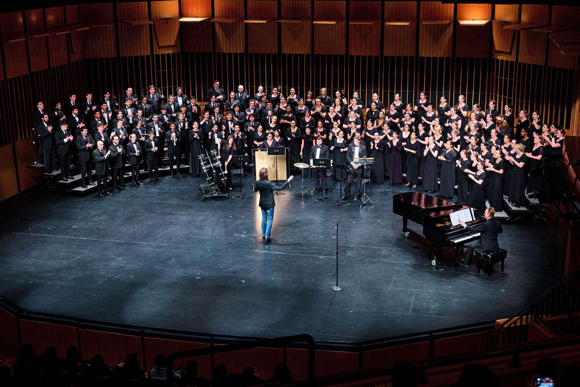 A chorus on stage with a man conducting.