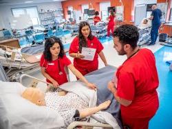 穿着红色手术服的学生聚集在医疗床上的人体模型周围