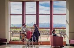 Three students sitting by large window in CELS building overlooking the NY skyline.