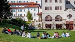 A teacher st和ing 和 students sitting on grass at Montclair State University Feliciano School of Business at Spring